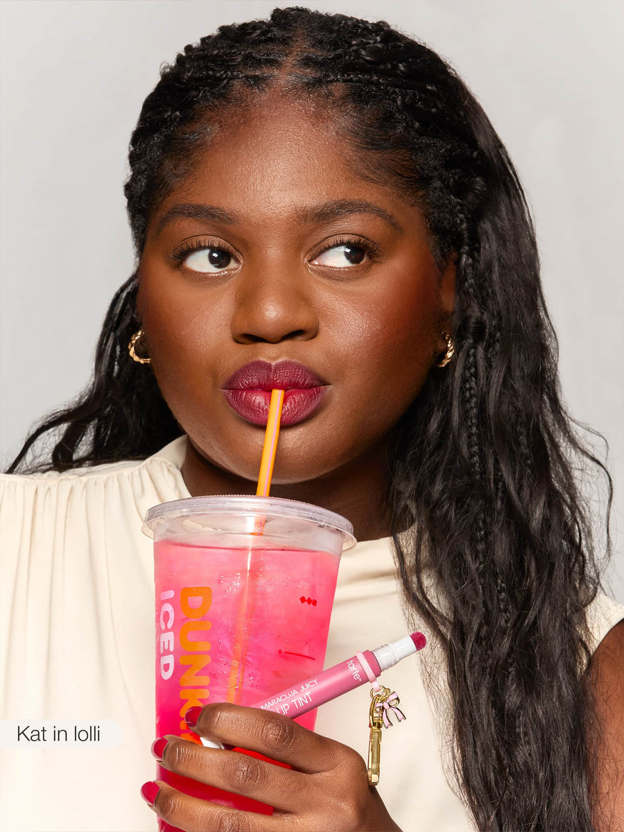A woman drinks from a pink beverage in a clear cup with an orange straw, holding a pink Tarte Cosmetics Maracuja Juicy Lip Tint. Text reads, Kat in lolli.