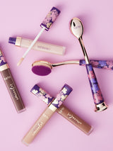 Makeup products including lip glosses and a brush on a pink background