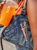 Person holding a Dunkin' iced coffee cup with a denim bag and pink lip gloss.