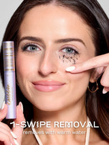 Woman applying makeup remover to tartelette tubing mascara with text '1-Swipe Removal' on a neutral background